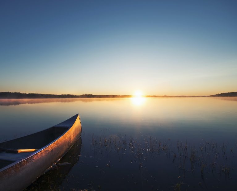 A canoe on a flat calm lake at sunset.