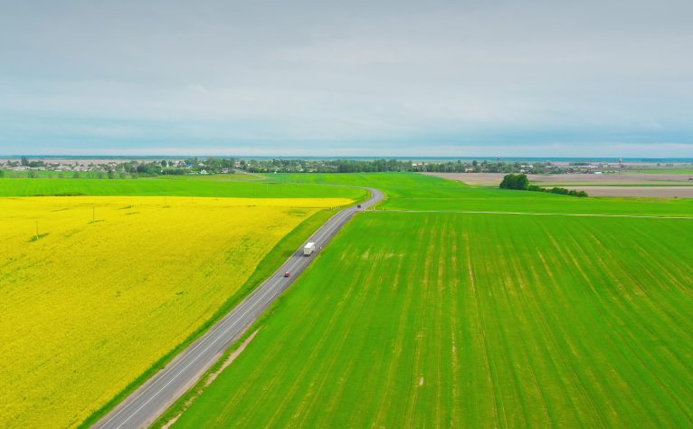 Aerial View Of Highway Road Through Field And Summer Wheat Fields Landscape. Top View Of Truck