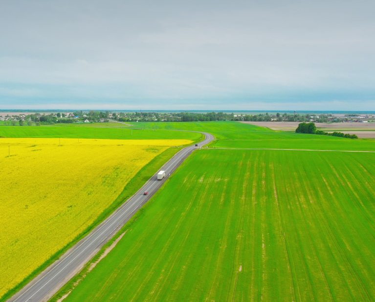 Aerial View Of Highway Road Through Field And Summer Wheat Fields Landscape. Top View Of Truck
